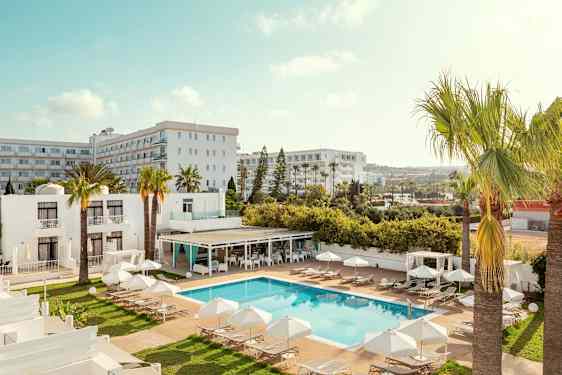 Et hotellområde med basseng, solsenger og parasoller, omgitt av palmer og bygninger. (AI-generert tekst)