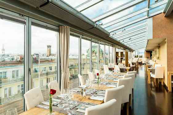 En lys restaurant med glassvegger og glass tak, bordene er dekket med hvite stoler og en rose på hvert bord. (AI-generert tekst)