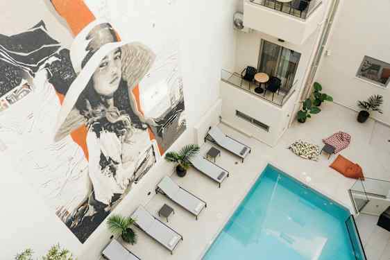 Bilde av et basseng omgitt av solsenger og sittesekker, med et stort veggmaleri. (AI-generert tekst)