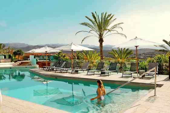 Bassengområde med solsenger og parasoller, omgitt av palmer og med utsikt over landskapet. (AI-generert tekst)