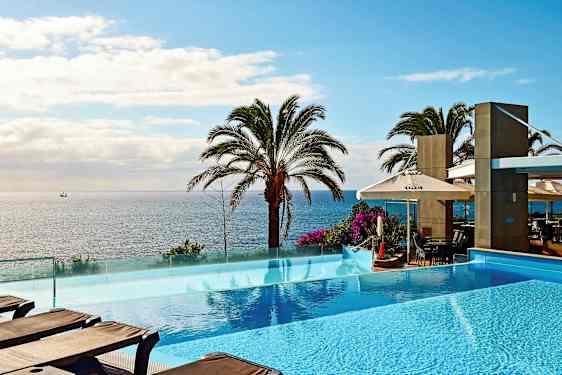 Bildet viser et infinity-basseng foran en havutsikt med palmer. (AI-generert tekst)