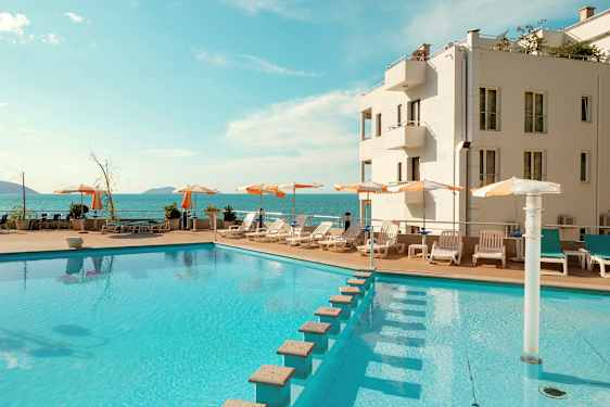 Et basseng med solsenger og parasoller ved et hotell, med havutsikt. (AI-generert tekst)