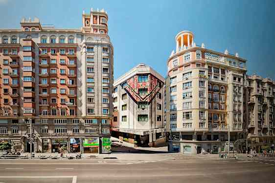 Tre bygninger ligger langs en gate, hvor midtbygningen har fargerike kunstverk på fasaden. (AI-generert tekst)