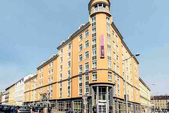 En lysgul bygning med mange vinduer, et skilt og buet hjørnefasade. (AI-generert tekst)