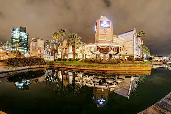 Hotell og bygninger ved en vannkanal om natten med speilrefleksjoner i vannet. (AI-generert tekst)