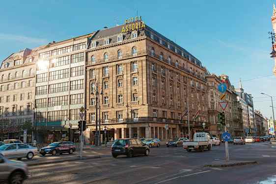 Et stort hotell i en historisk bygning med skiltet "Hotel Astoria" synlig på taket. Foran bygningen er et veikryss med trafikk. (AI-generert tekst)