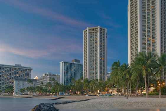 Høye bygninger ved en strand med palmer i skumringen. (AI-generert tekst)