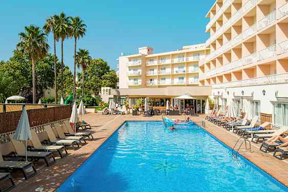 Et hotellbygg ligger ved siden av et utendørsbasseng med solsenger og parasoller rundt. (AI-generert tekst)