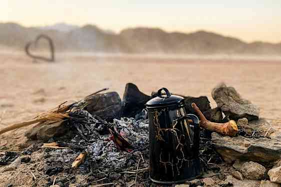 En kaffekanne står ved et utbrent bål i et ørkenlandskap. (AI-generert tekst)