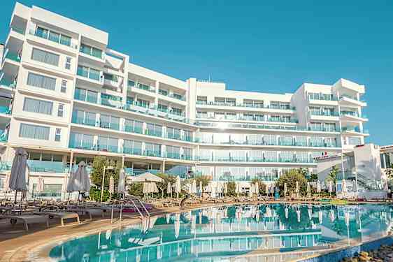 Hvit bygning med flere etasjer og balkonger, foran et basseng omgitt av solsenger og parasoller. (AI-generert tekst)