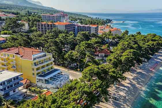 Luftfoto av en strand med solsenger og parasoller ved siden av hotellbygninger og grøntområder. (AI-generert tekst)
