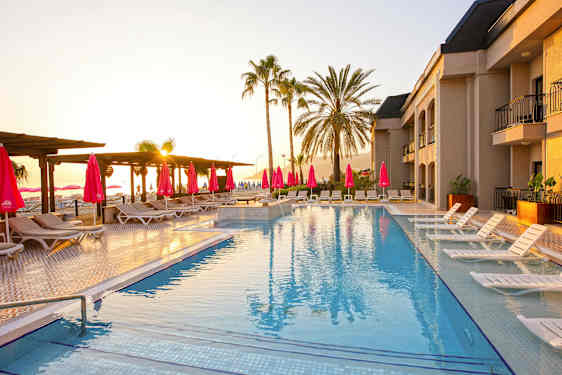 Basseng med solsenger og parasoller, omgitt av palmer ved solnedgang. (AI-generert tekst)