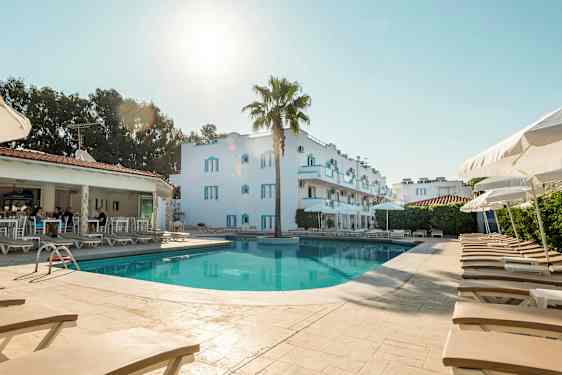 Bilde av et basseng med solsenger og parasoller, bak ses en hvit bygning og et åpent reservasjonsområde. (AI-generert tekst)