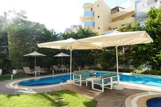 Utendørs basseng med solsenger og parasoller, omgitt av trær og bygninger. (AI-generert tekst)