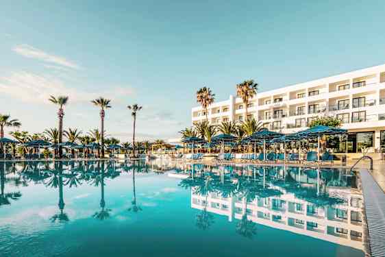 Eksteriør av et hotell med et stort basseng foran og omkransende palmer. (AI-generert tekst)