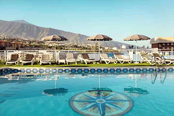 Bassengområde med solsenger og parasoller med utsikt over fjell og bygninger. (AI-generert tekst)