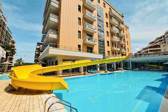 En bygning med balkonger ved siden av et basseng med en gul vannsklie. (AI-generert tekst)