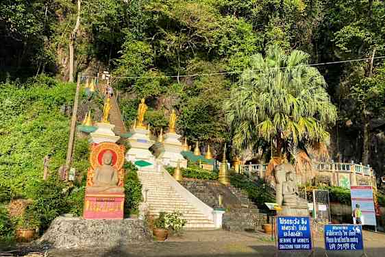 Bilde av en trapp som fører opp til flere gyldne buddhistiske statuer og strukturer omgitt av vegetasjon. (AI-generert tekst)