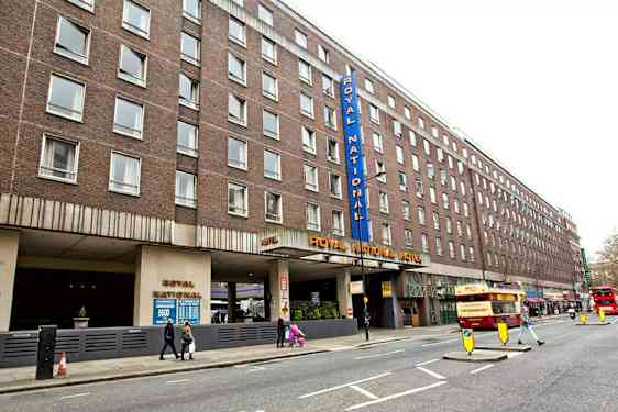 Bilde av Royal National Hotel fra gaten med flere busser og fotgjengere. (AI-generert tekst)