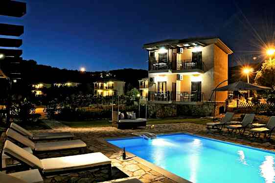 Et kveldsbilde av et utendørsbasseng og flere solsenger. I bakgrunnen vises et hus med balkonger og omgivende belysning. (AI-generert tekst)