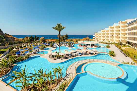 Bilde av et hotellområde med store bassenger og omkringliggende solsenger, samt havutsikt i bakgrunnen. (AI-generert tekst)