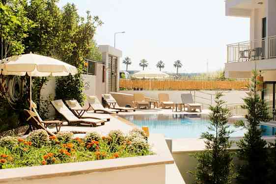 Et basseng omgitt av solsenger, parasoller og grøntområder. (AI-generert tekst)