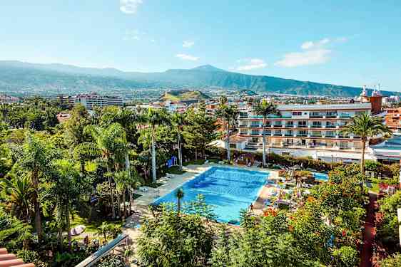 Et basseng omgitt av planter og bygninger med et fjell i bakgrunnen. (AI-generert tekst)