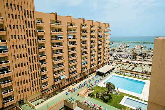 En høy bygning med balkonger og et basseng foran samt en marina i bakgrunnen. (AI-generert tekst)