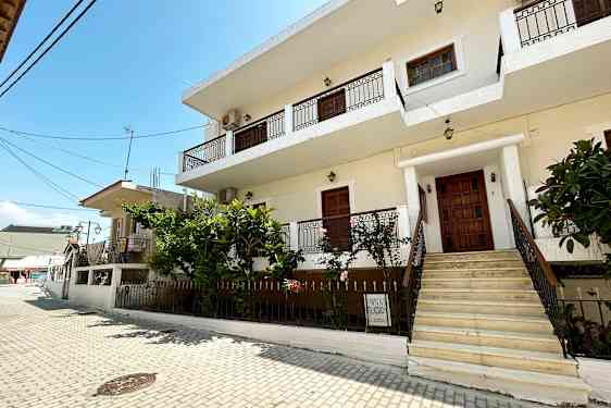 En hvit bygning med balkonger og en trapp opp fra en brosteinsbelagt gate. (AI-generert tekst)