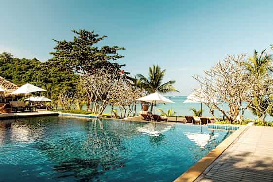 Et infinitybasseng ved en strand med solsenger og parasoller i bakgrunnen. (AI-generert tekst)