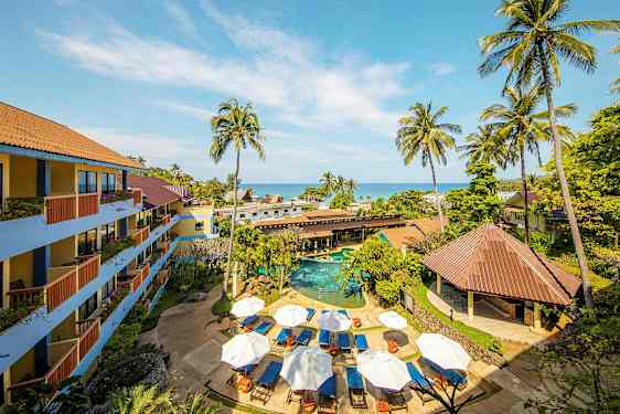 Flere bygninger ved et basseng med solsenger og parasoller, omgitt av palmer og grøntområder. (AI-generert tekst)