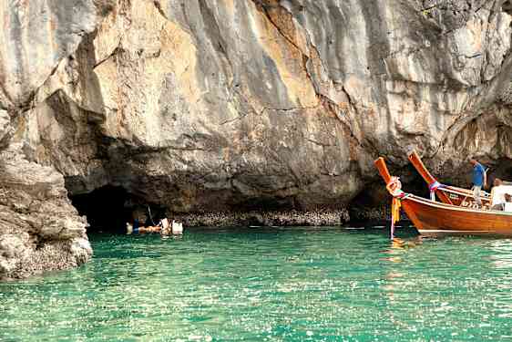 Personer svømmer i vannet ved en klippe, og to trefartøyer flyter nært. (AI-generert tekst)