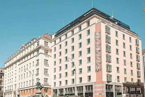 Et bymiljø med flere bygninger, inkludert et hotell med skiltet "Hotel Europa", under en klar blå himmel. (AI-generert tekst)