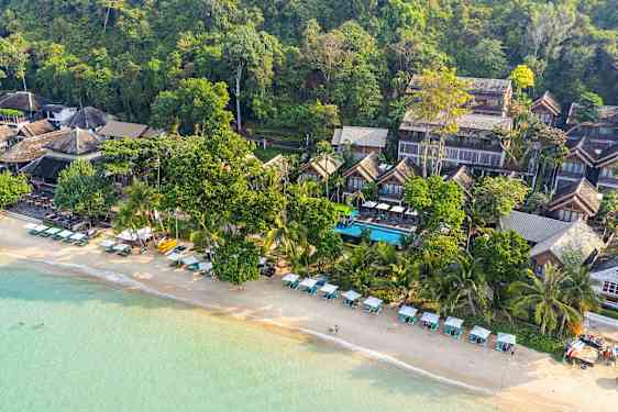 Luftfoto av en strand med solsenger og parasoller samt bygninger omgitt av grøntområder. (AI-generert tekst)