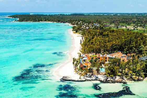 En sandstrand med turkist vann og hotell omgitt av grøntområde. (AI-generert tekst)