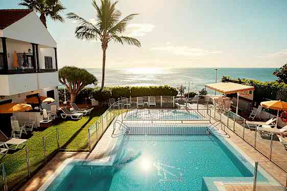 Et utendørs svømmebasseng med solsenger og parasoller ved siden av, med havet i bakgrunnen. (AI-generert tekst)