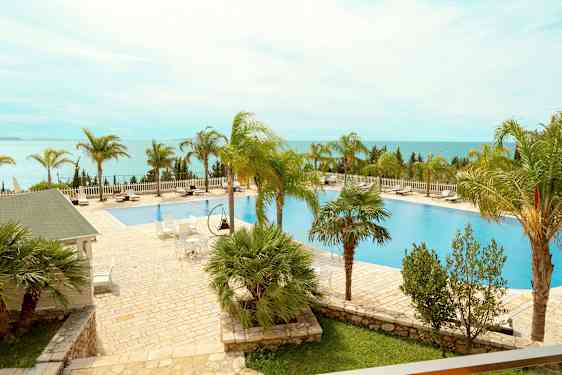 Et utendørsbasseng med omkringliggende solsenger og palmer med utsikt over havet. (AI-generert tekst)