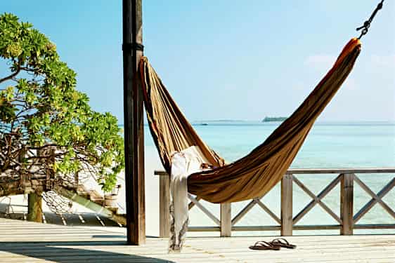 En hengekøye henger mellom to stolper på en veranda med utsikt over turkis hav. (AI-generert tekst)