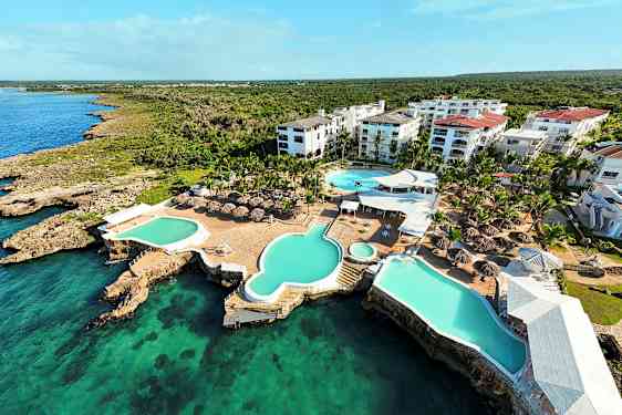 Luftfoto av et feriested med bassenger og takparasoller ved sjøen. (AI-generert tekst)