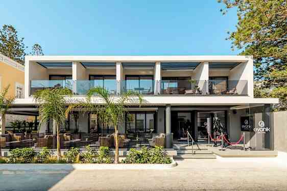 Moderne hotellbygning med glassrekkverk og utemøbler ved inngangen. (AI-generert tekst)