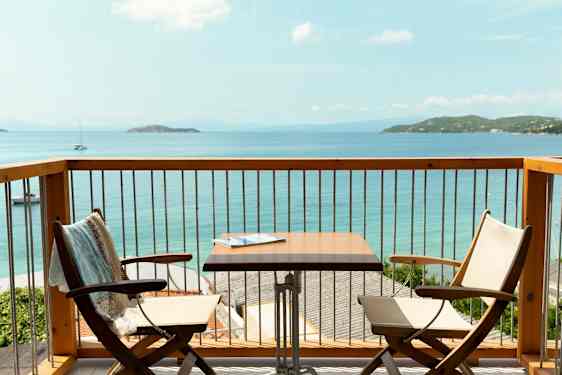Utsikt fra en balkong med to stoler, et bord og havet i bakgrunnen. (AI-generert tekst)
