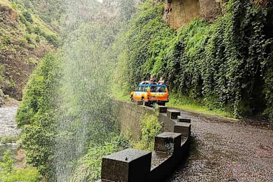 En gul-oransje jeep på en vei ved et fossefall i en grønn dal. (AI-generert tekst)