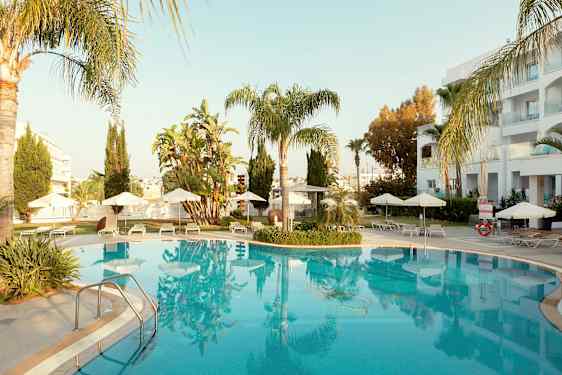 Utendørs svømmebasseng omgitt av solsenger og parasoller, med palmer og bygninger i bakgrunnen. (AI-generert tekst)