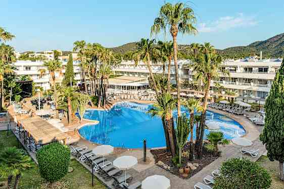 Et hotellbasseng omgitt av solsenger og parasoller, med palmer og bygninger i bakgrunnen. (AI-generert tekst)