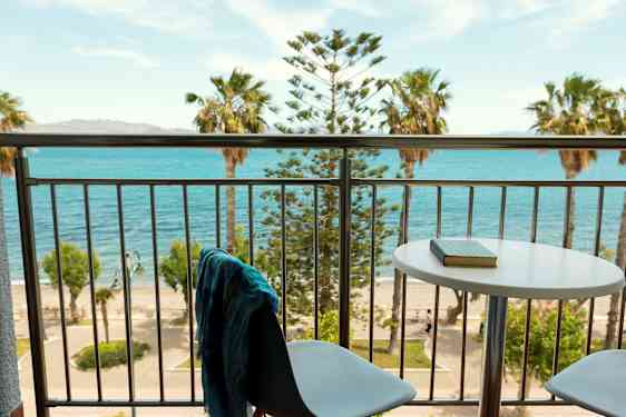 Utsikt fra en balkong med bord og stoler mot havet og palmer. (AI-generert tekst)