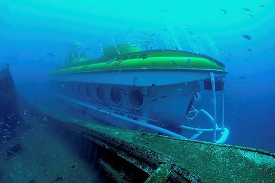 Undervannsvy av en ubåt ved siden av et gammelt skipsvrak omgitt av fisk. (AI-generert tekst)