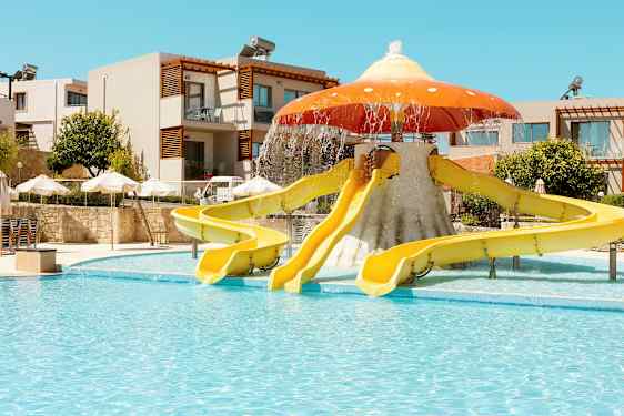 Vannsklier formet som en sopp ved et utendørs basseng; bygninger og parasoller i bakgrunnen. (AI-generert tekst)