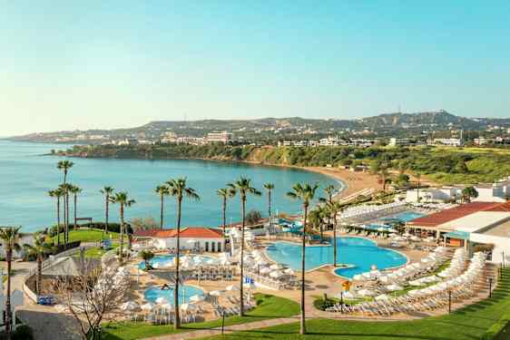 Utsikt over hotellområde med bassenger og utsikt mot en bukt med blått vann og grønne omgivelser. (AI-generert tekst)