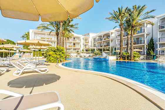 Et utendørs basseng omgitt av solsenger og parasoller med hotellbygninger i bakgrunnen. (AI-generert tekst)