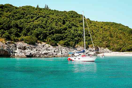Seilbåt på turkis vann nær en frodig strand. (AI-generert tekst)